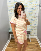 A woman takes a mirror selfie wearing a matching two-piece lounge set with light pink and white horizontal stripes. The set includes a short-sleeve top and shorts with solid pink trim and a pink drawstring.