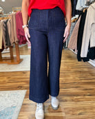 Person wearing dark blue wide-leg jeans and a red top in a clothing store.