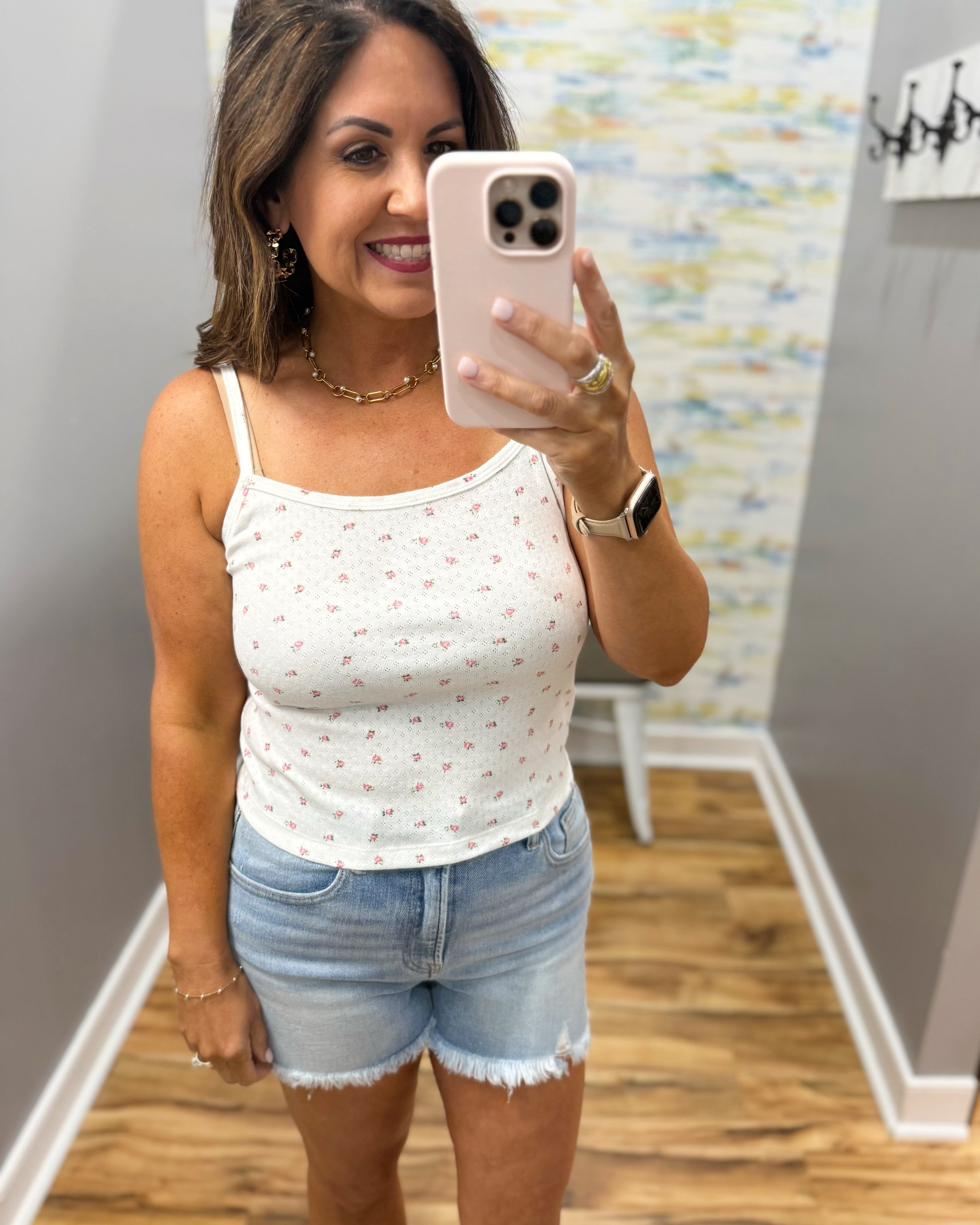 woman wearing white floral cami top with denim shorts.