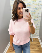 Woman taking a mirror selfie wearing a pink sweater and blue jeans in a room with a colorful wall.