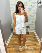 woman wearing a white top with blue palm trees embroidered on it.