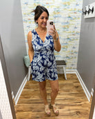 Woman taking a mirror selfie wearing a blue and white floral dress in a room with a patterned wall.