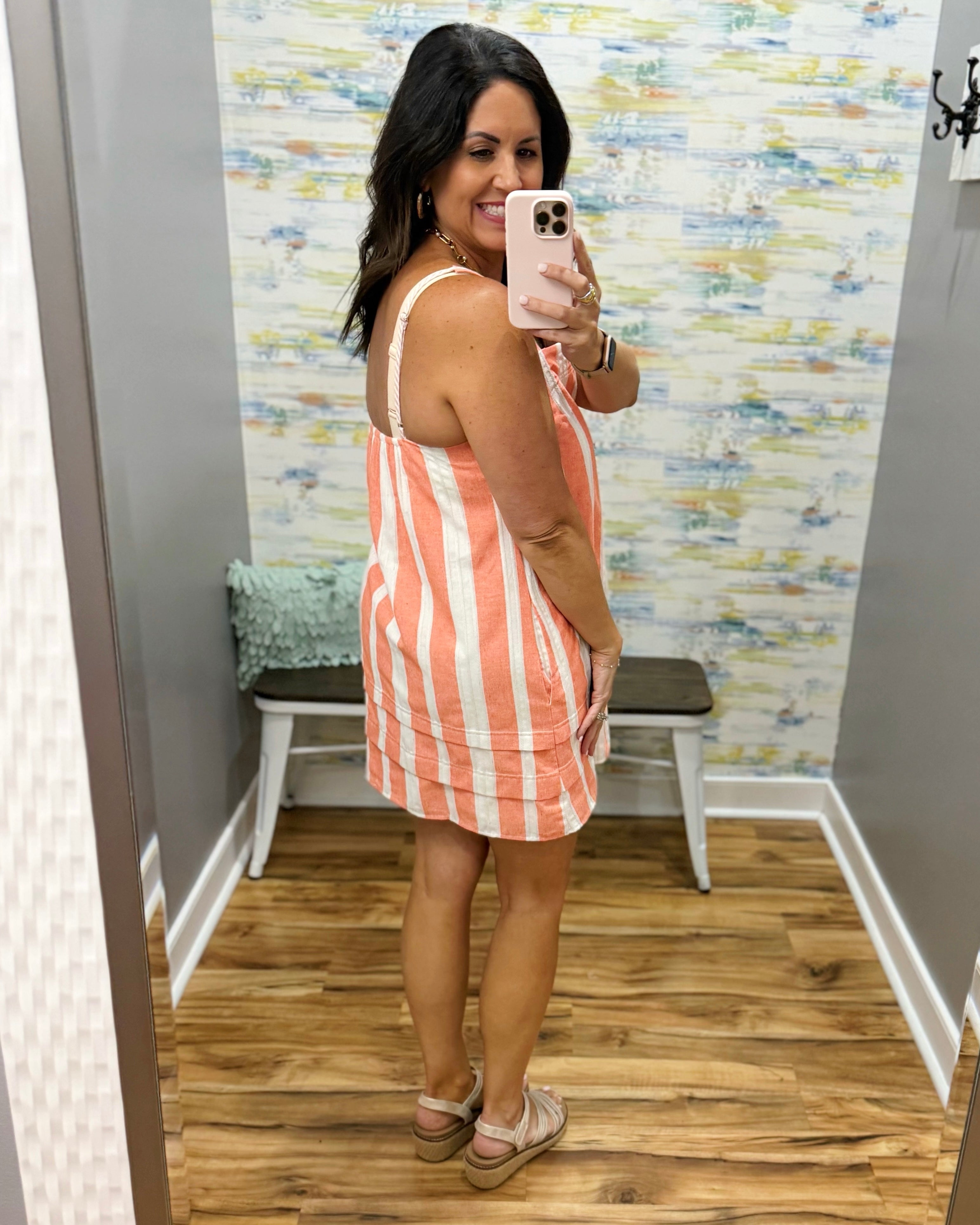 Woman taking a mirror selfie wearing an orange and white striped dress in a room with a textured wall.