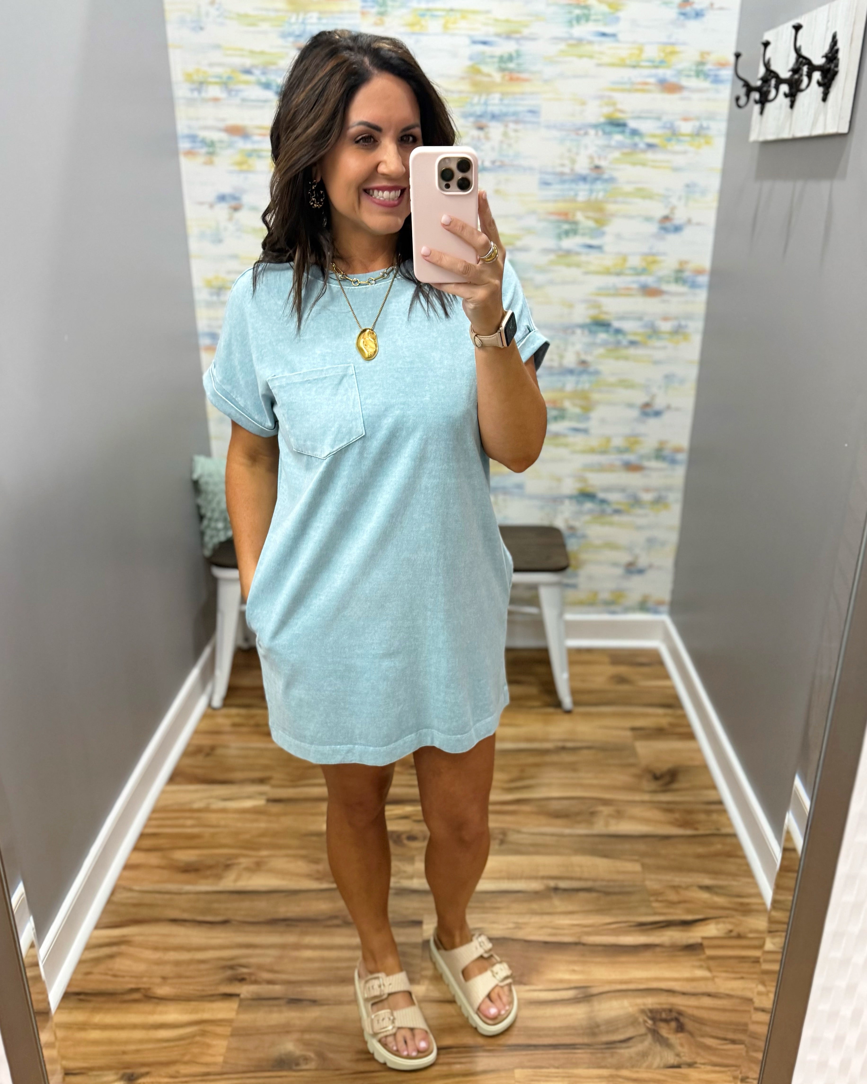 Woman taking a mirror selfie wearing a light blue dress in a room with a patterned wall.