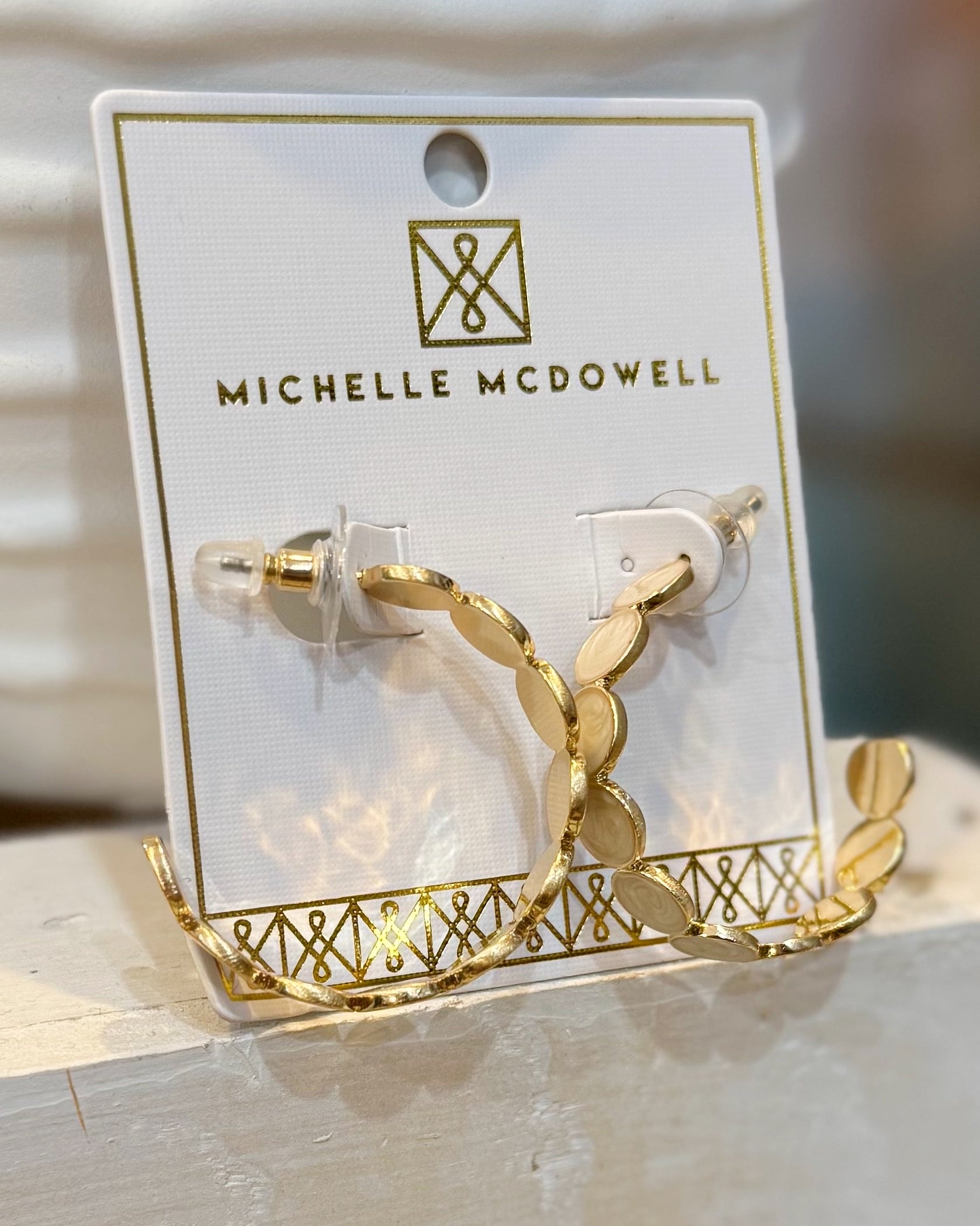 Gold hoop earrings on a branded card with 'Michelle McDowell' on a wooden surface.