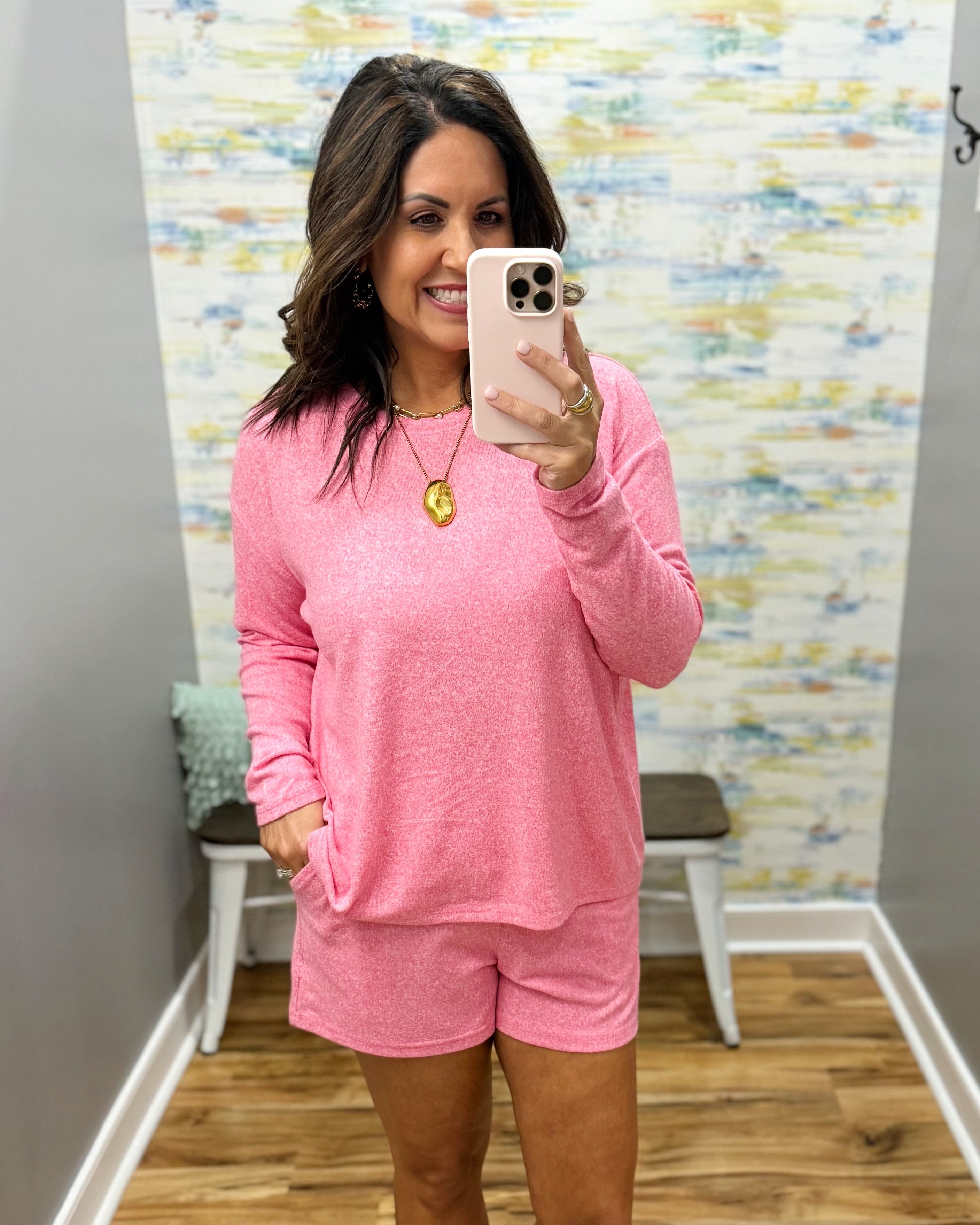 Woman taking a mirror selfie wearing a pink outfit in a room with a colorful wall.