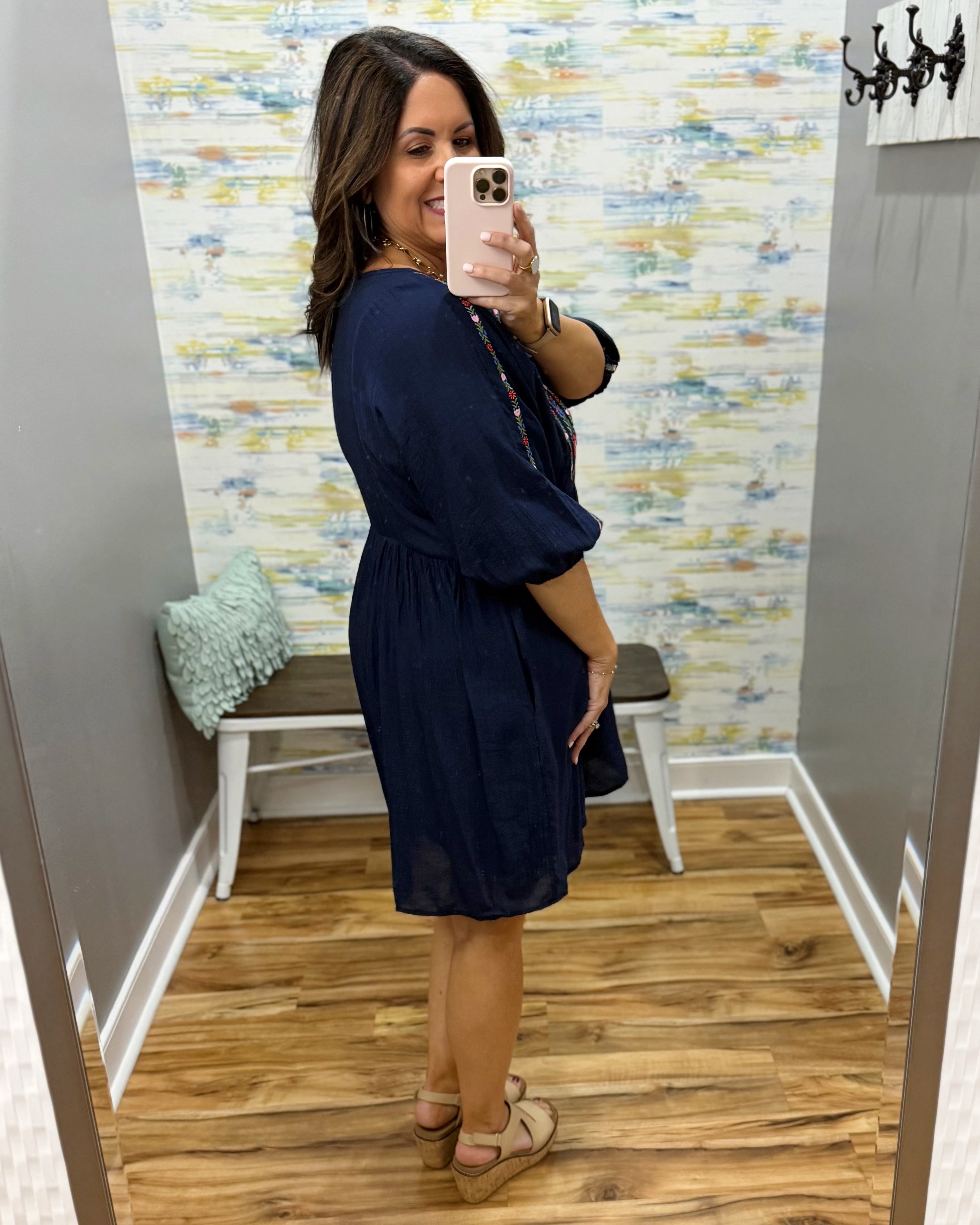 Woman taking a mirror selfie wearing a navy blue dress in a room with patterned wallpaper.