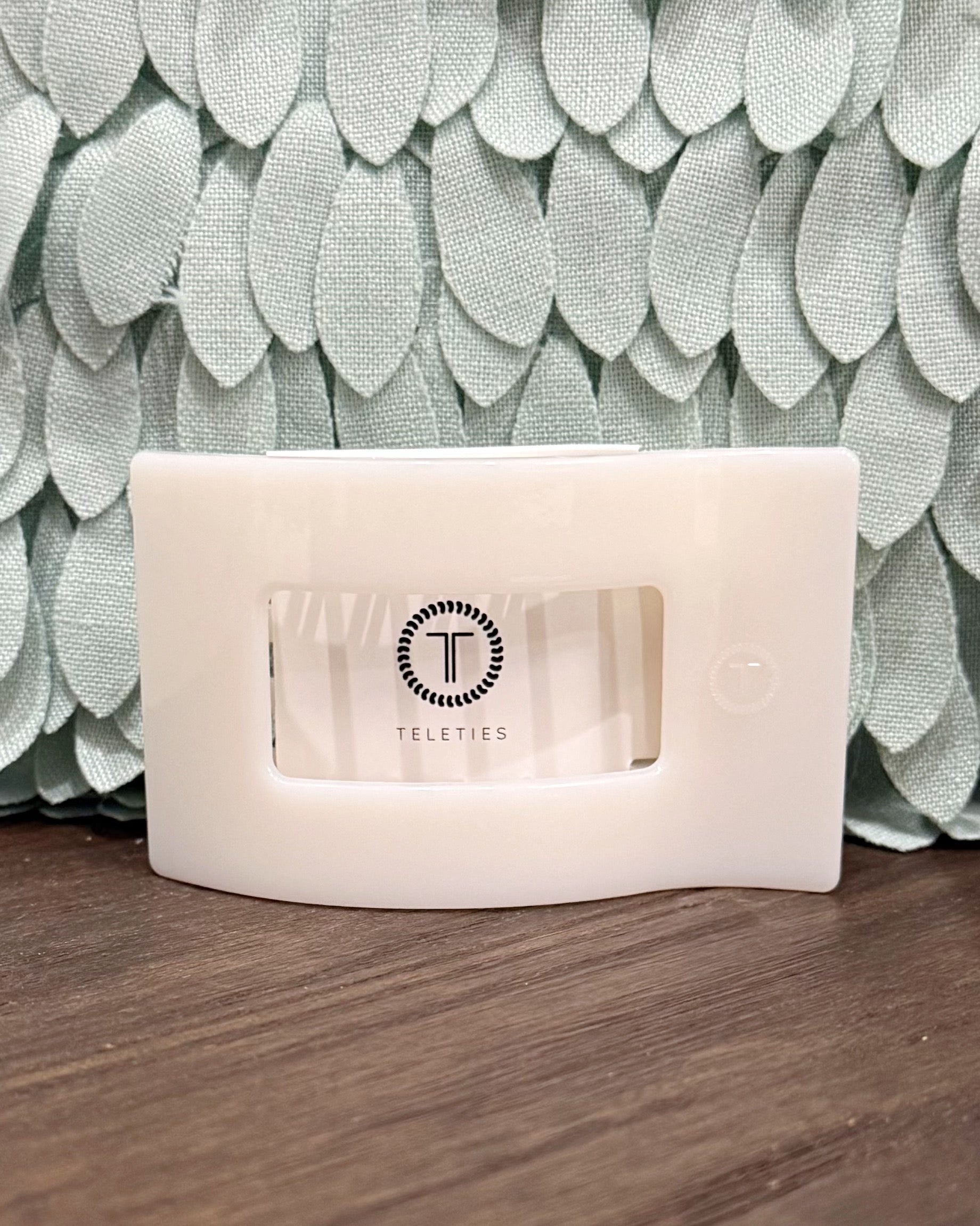 White electronic device with 'Teleties' branding on a wooden surface with a textured green wall background