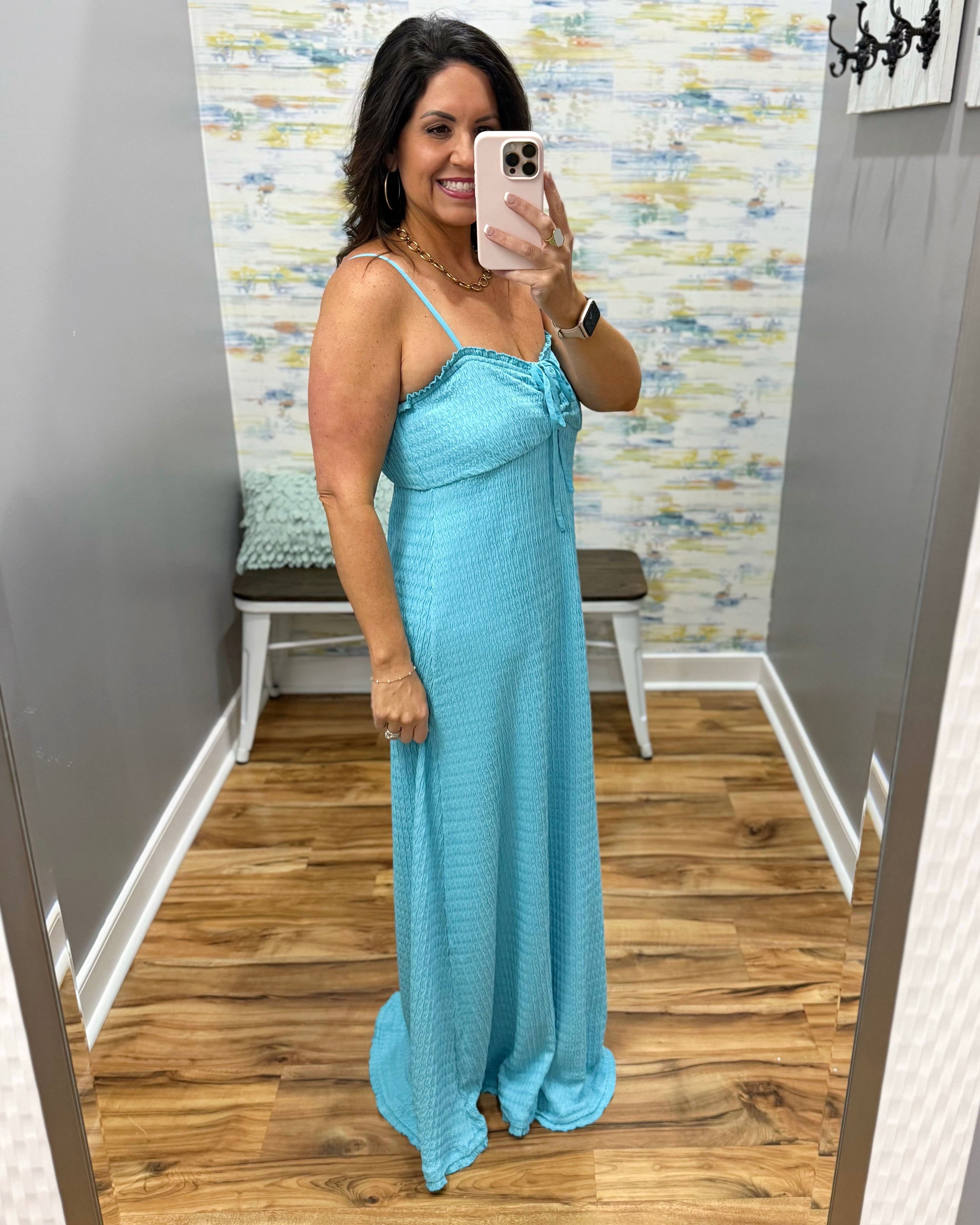 Woman taking a mirror selfie wearing a blue dress in a room with a patterned wall.