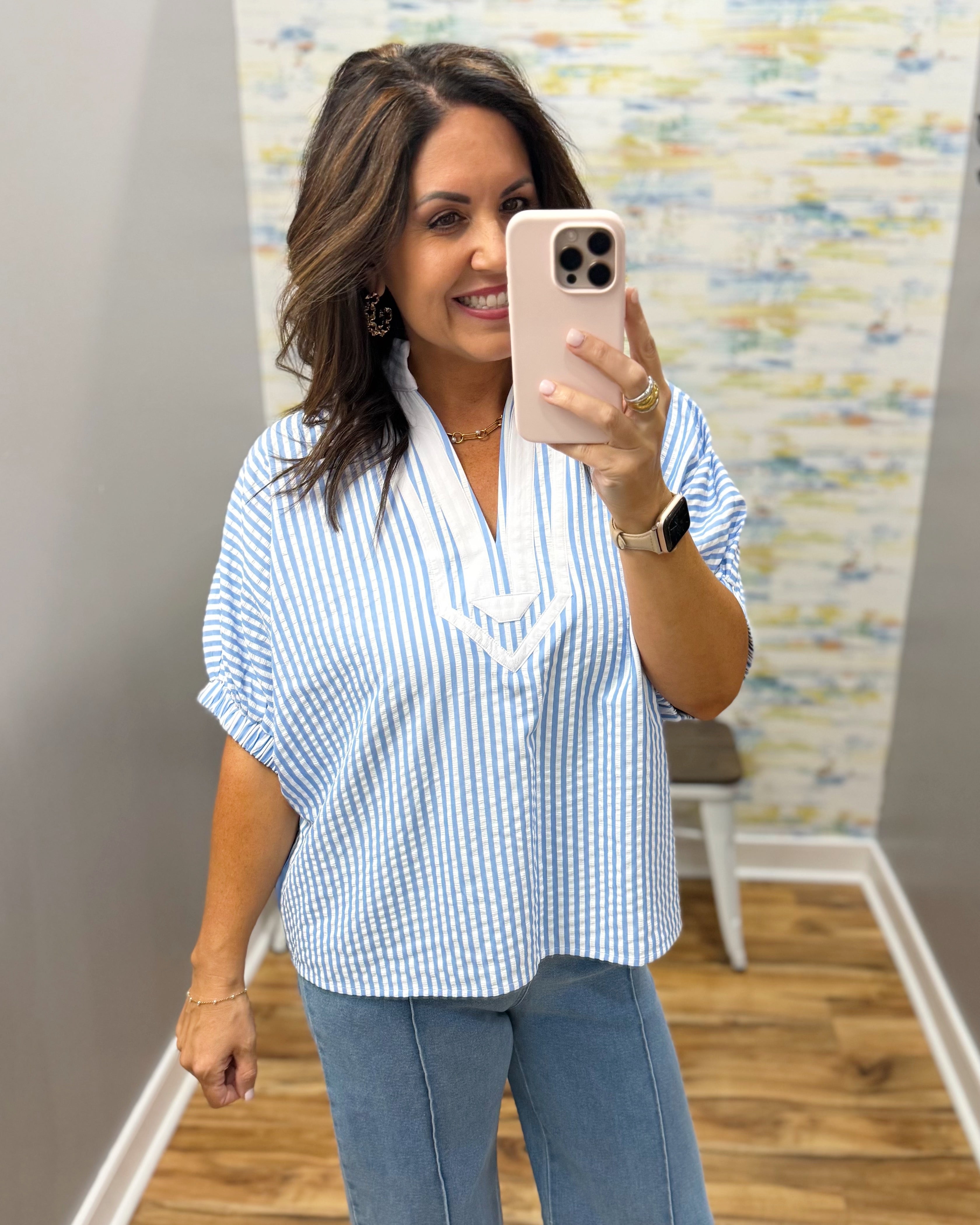 Woman taking a mirror selfie wearing a blue and white striped shirt and jeans.