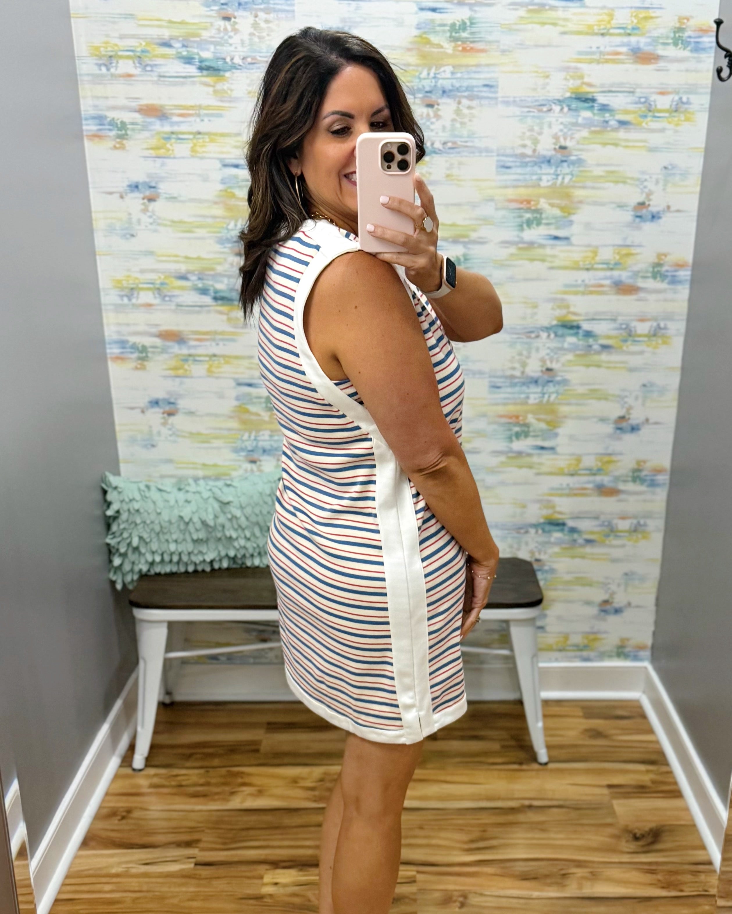 Woman taking a mirror selfie wearing a striped dress in a room with colorful wall paper.