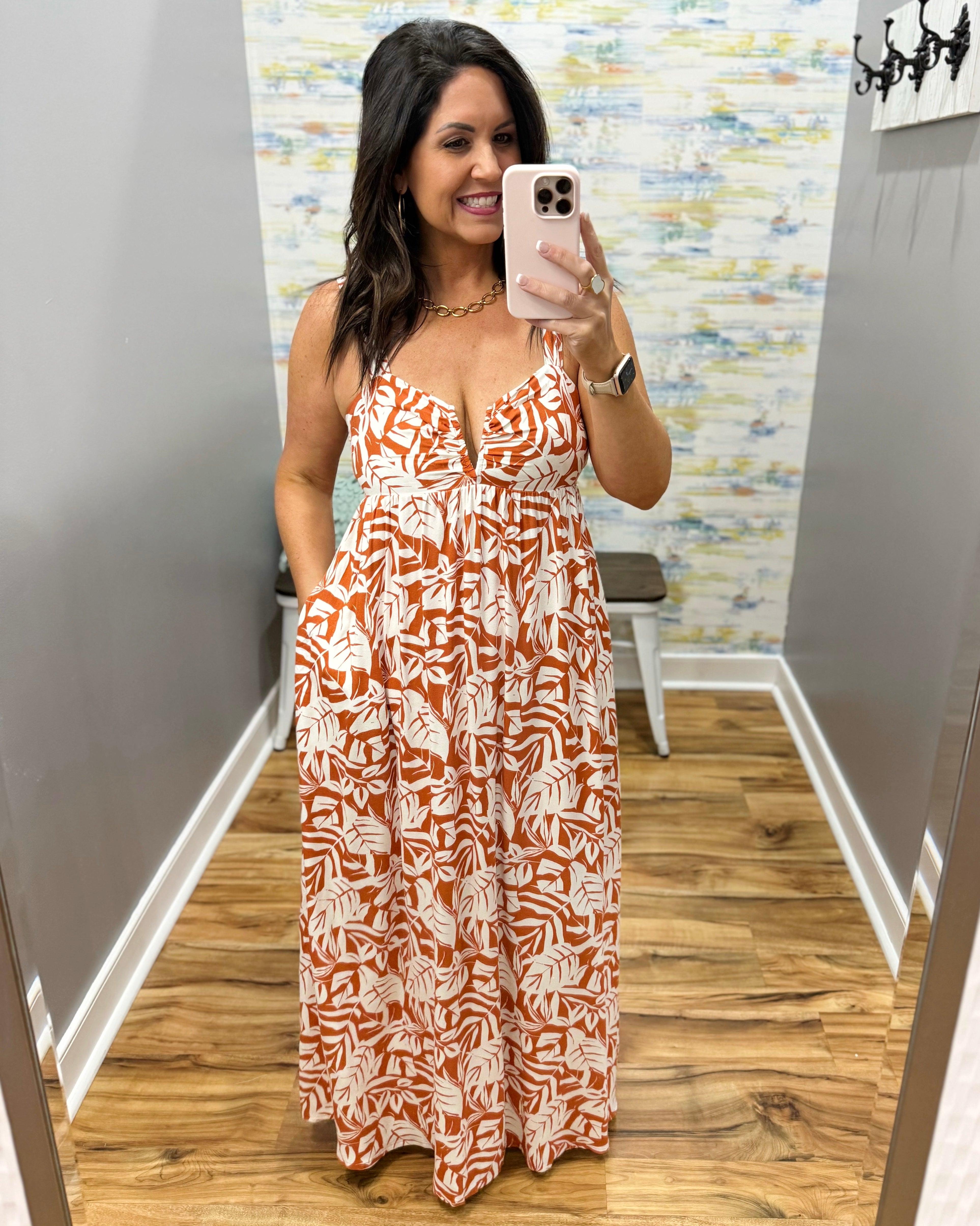 Woman taking a mirror selfie wearing a patterned dress in a room with a colorful wall.
