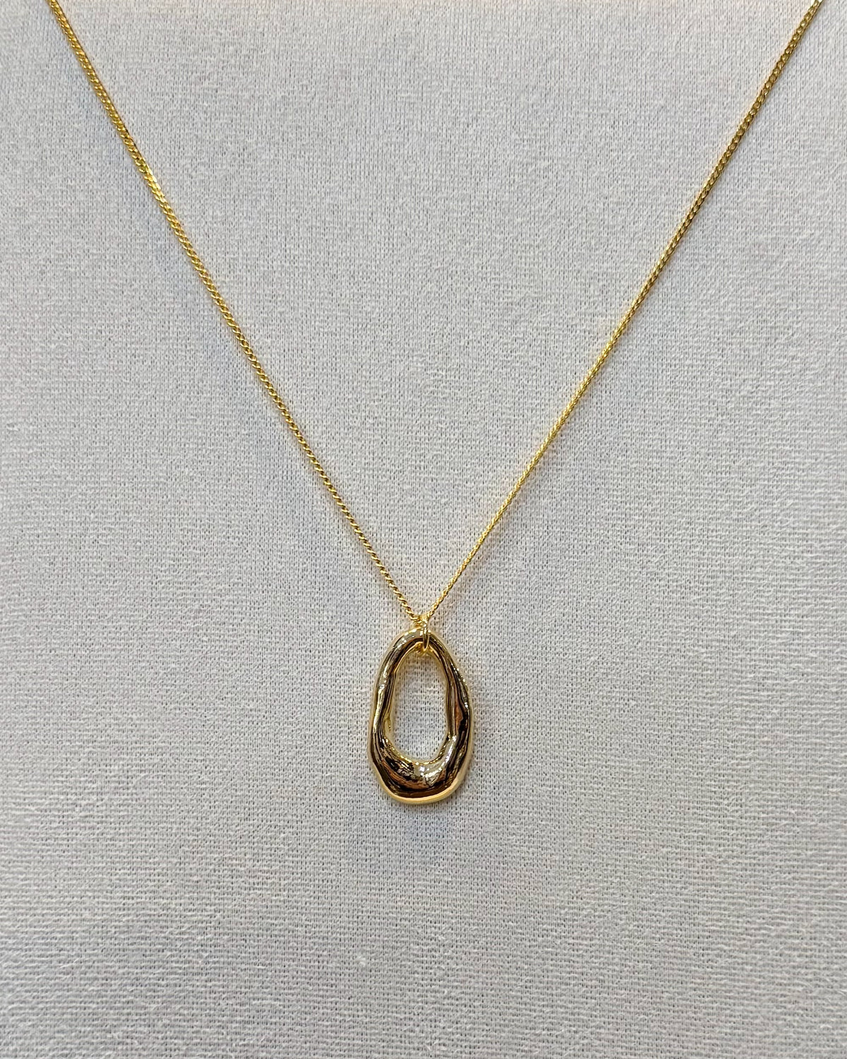 This organic oval open ring pendant necklace features a sculpted elongated oval ring with a molten wavy edge hanging from a fine gold tone chain.