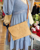 Person wearing a blue dress with a straw handbag in a store setting