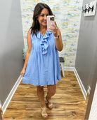 Woman taking a mirror selfie wearing a blue dress in a room with patterned wallpaper.