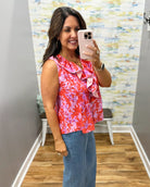 Woman taking a mirror selfie wearing a colorful sleeveless top and jeans in a room with a patterned wall.