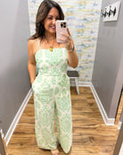 Woman taking a mirror selfie wearing a green floral jumpsuit in a room with a colorful wall.