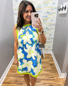Woman taking a mirror selfie wearing a floral dress in a room with a patterned wall.