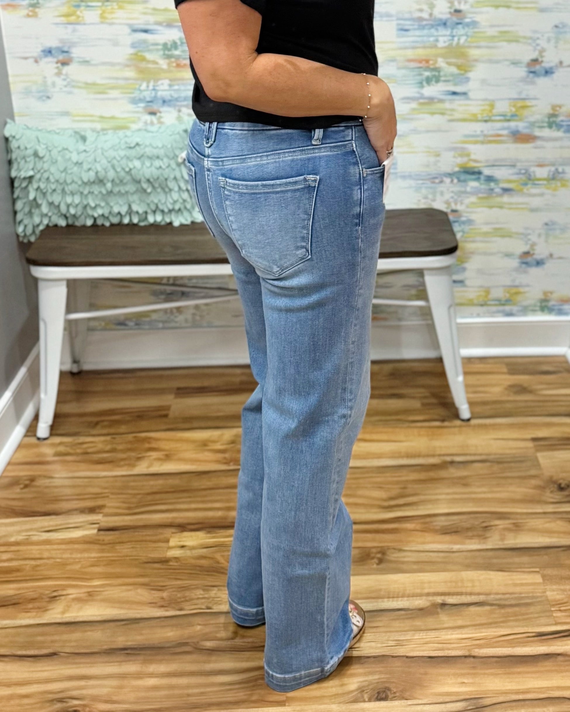 Person wearing blue jeans standing on a wooden floor with a colorful wall in the background