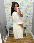 Woman taking a mirror selfie wearing a white dress in a room with colorful wall paper.