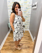 Woman taking a mirror selfie wearing a floral dress in a room with a colorful wall.