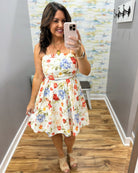 Woman taking a mirror selfie wearing a floral dress in a room with a patterned wall.