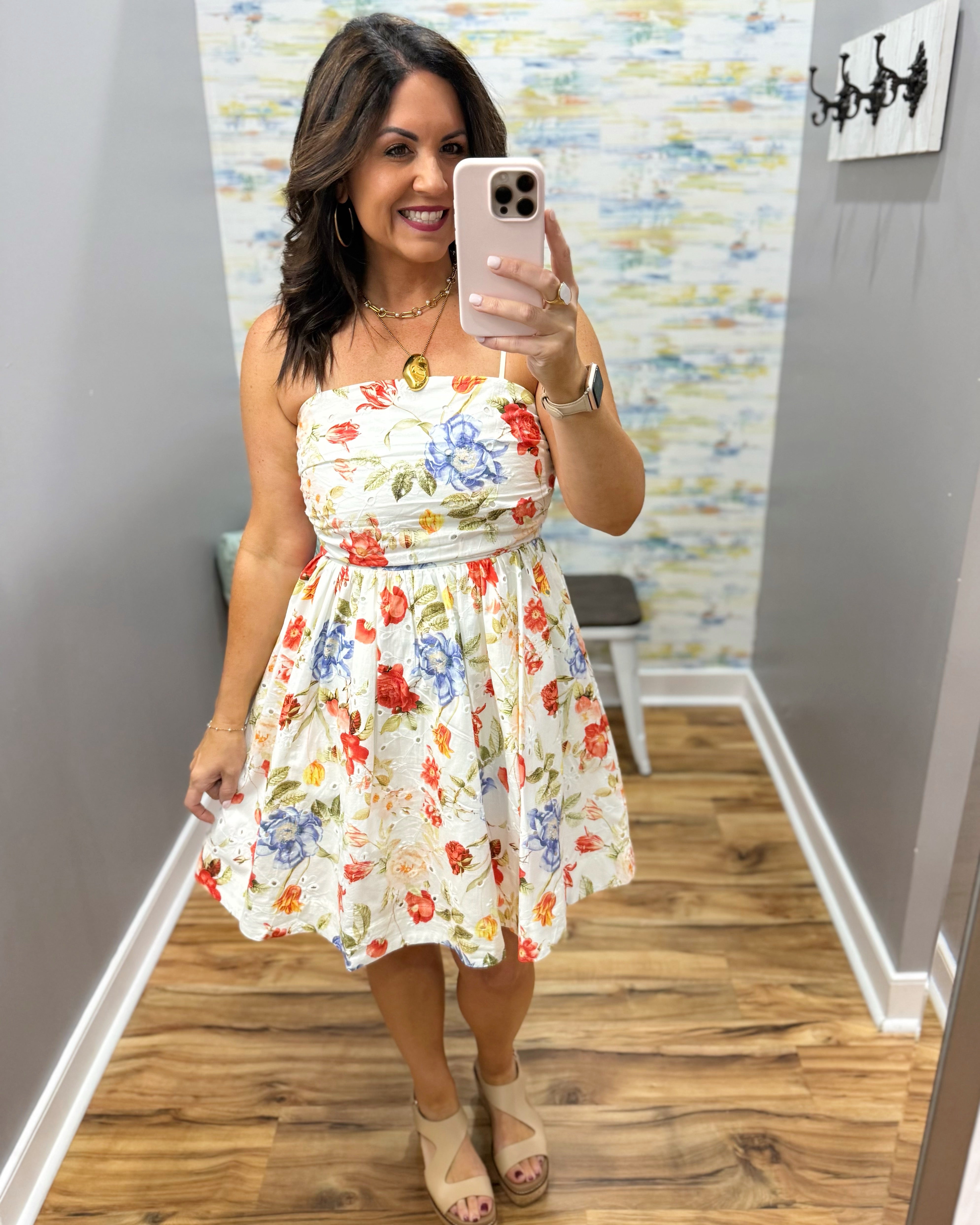 Woman taking a mirror selfie wearing a floral dress in a room with a patterned wall.