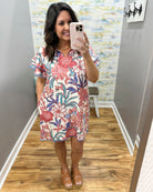Woman taking a mirror selfie wearing a floral dress in a room with a colorful wall.