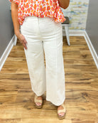 Person wearing a colorful top and white pants on a wooden floor.