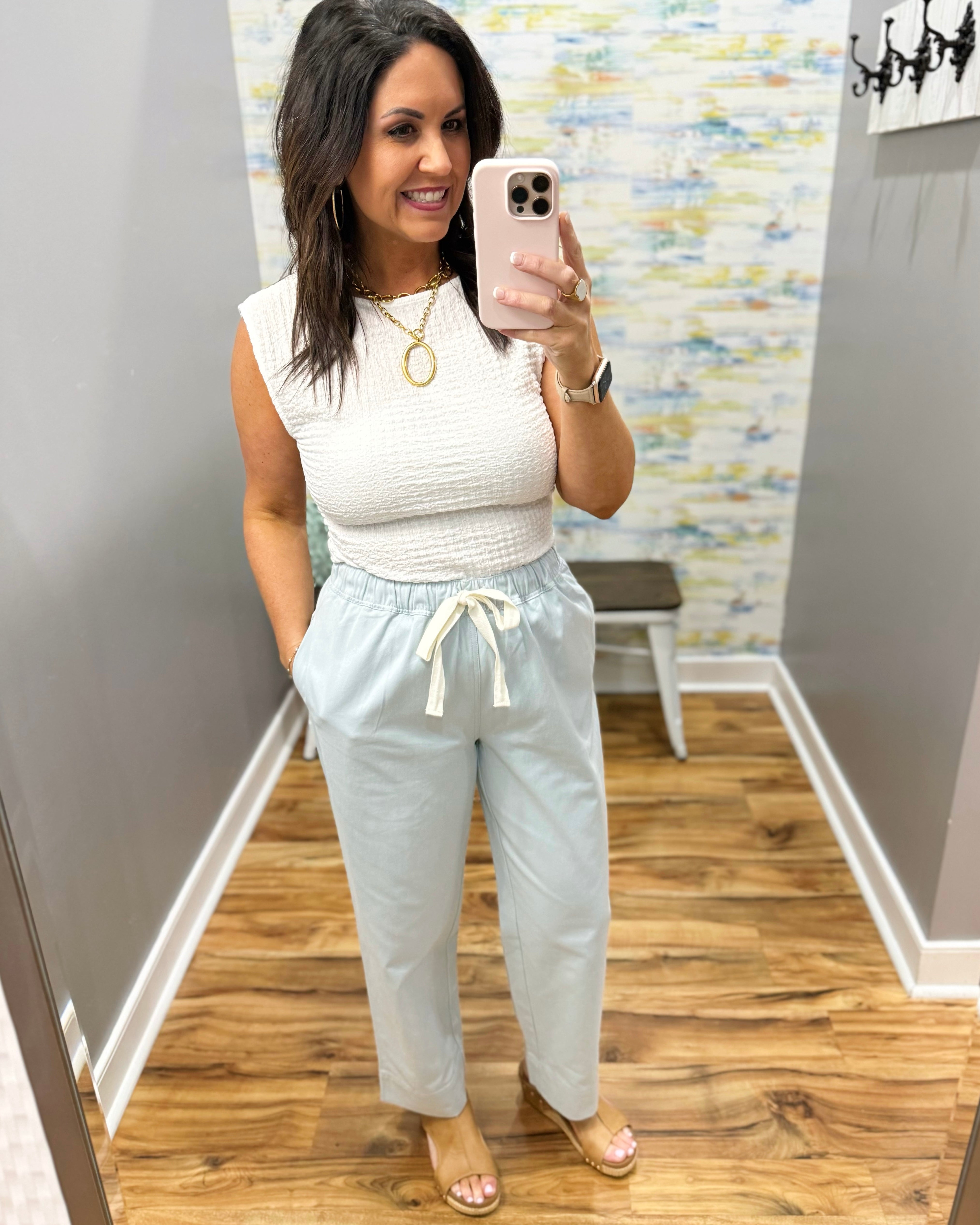 Woman wearing a white top and light blue pants in a room with a colorful wall.