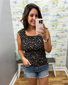Woman taking a mirror selfie wearing a black floral top and denim shorts in a room with colorful wall art.