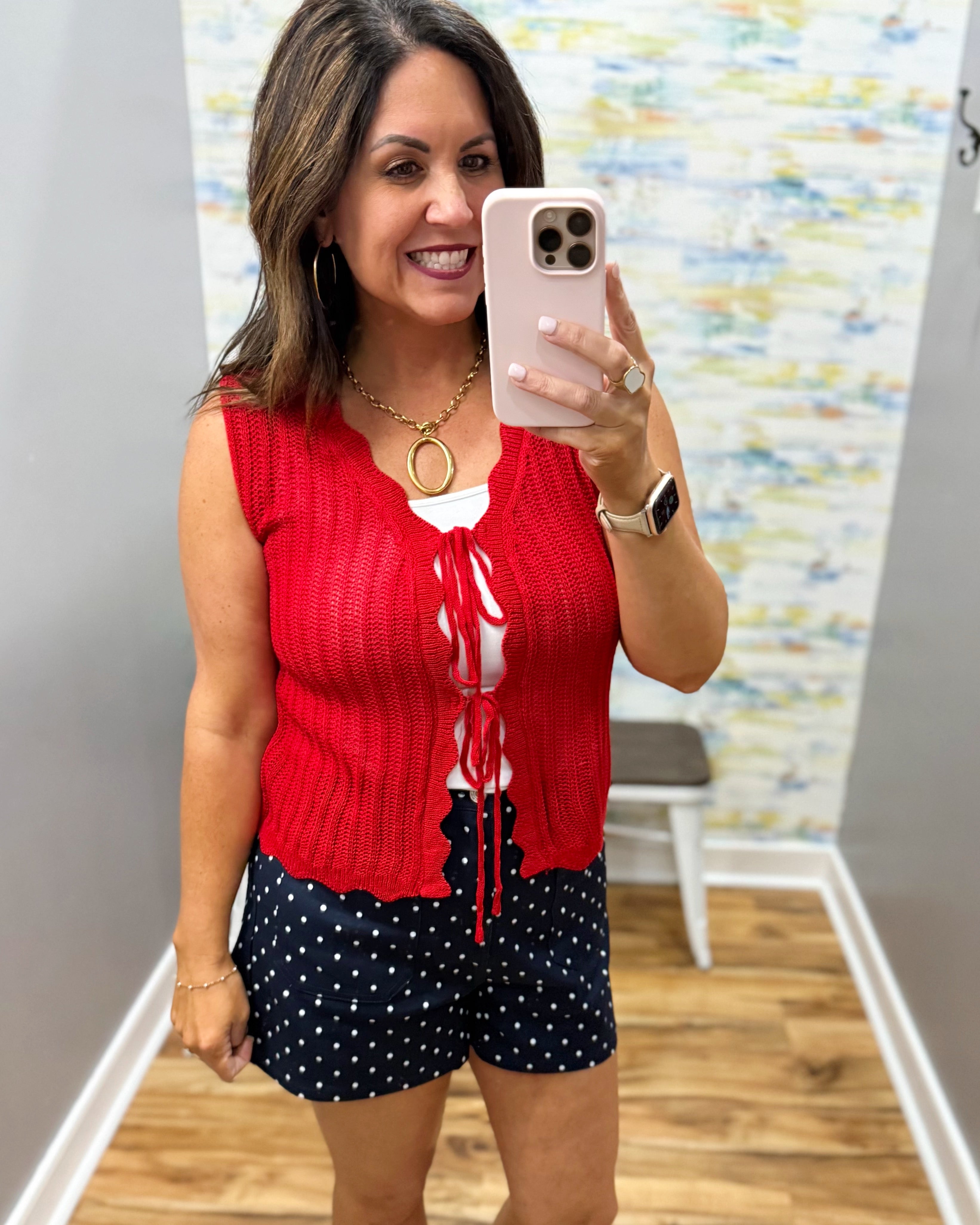 Woman taking a mirror selfie wearing a red top and navy polka dot shorts.