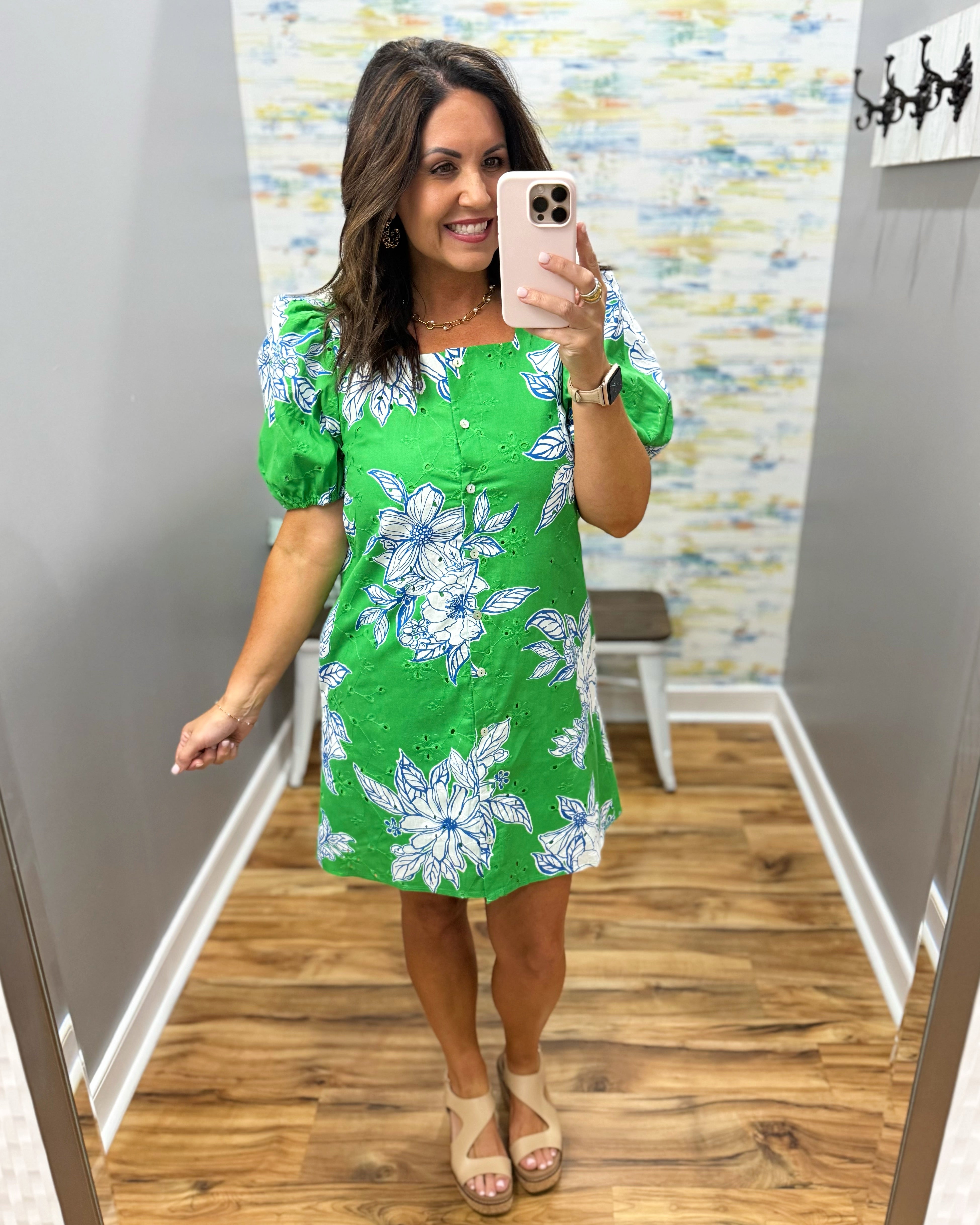 Woman taking a mirror selfie wearing a green floral dress in a room with a colorful wall.