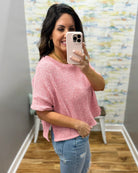 Woman taking a mirror selfie wearing a pink top and ripped jeans in a room with a colorful wall.