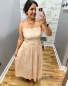 Woman taking a mirror selfie wearing a beige dress in a room with a patterned wall.