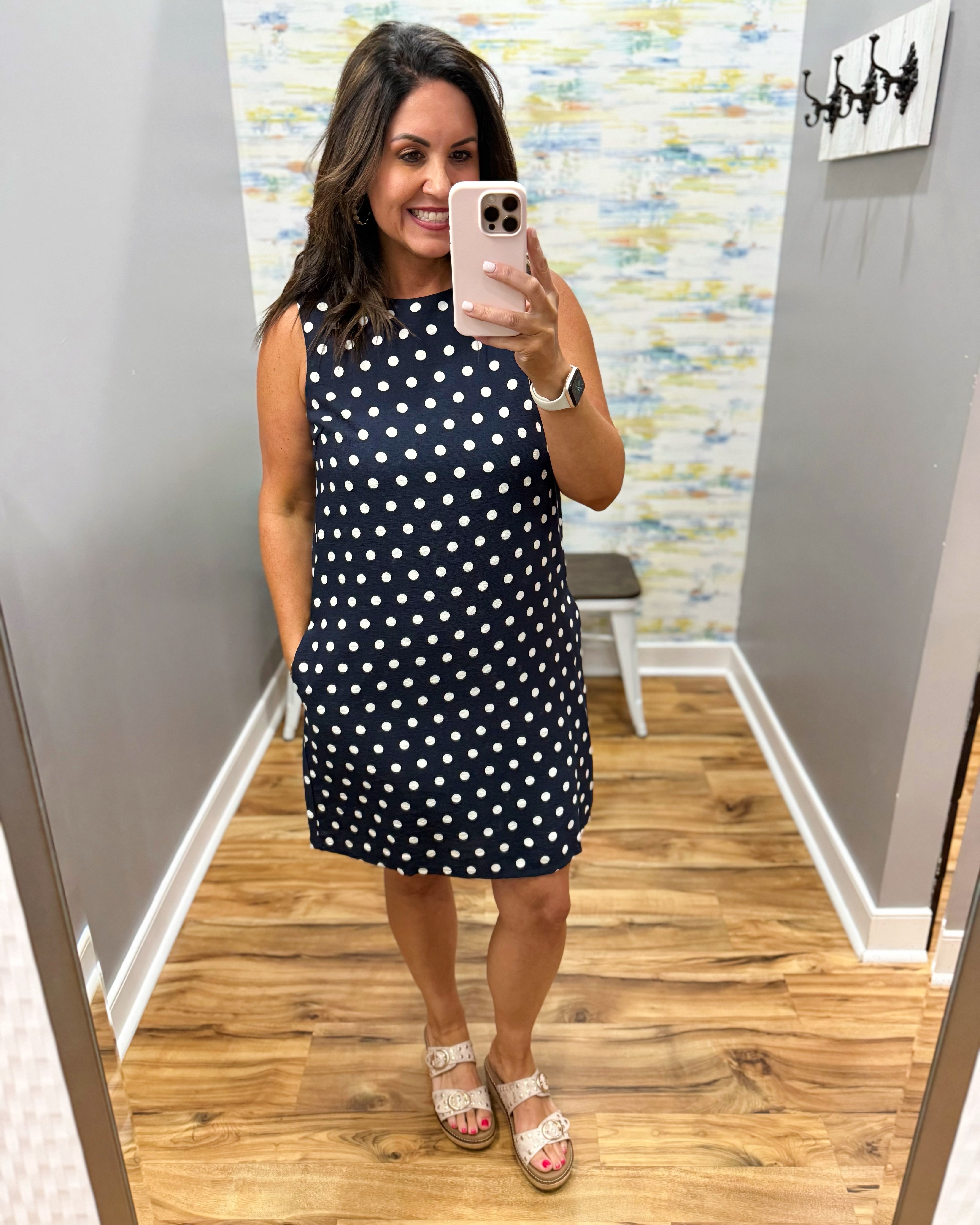 Woman taking a mirror selfie wearing a navy dress with white polka dots in a room with a colorful wall.