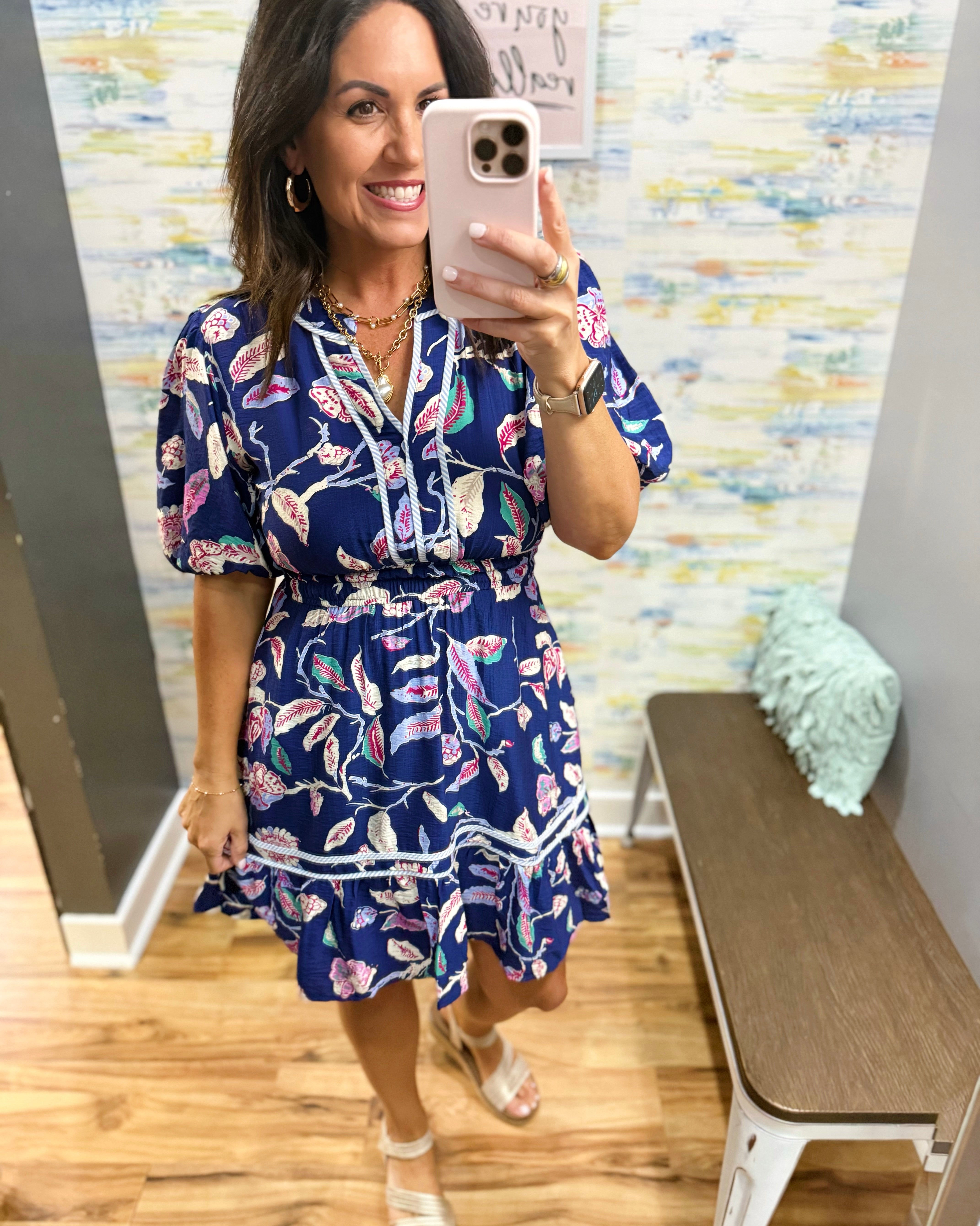 Woman taking a mirror selfie wearing a blue floral dress in a store.