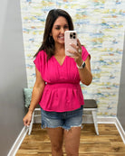 Woman taking a mirror selfie wearing a pink top and denim shorts in a room with a colorful wall.