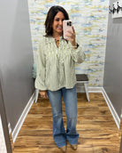 A woman takes a mirror selfie wearing a cream and green vertically striped long-sleeve blouse with a ruffled collar, paired with blue flare jeans and tan boots.