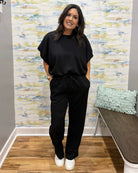 Woman in black outfit standing in a room with a textured wall and a chair.