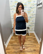 Woman taking a mirror selfie wearing a navy and white dress in a room with a patterned wall.