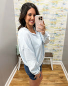 Woman taking a mirror selfie wearing a white sweatshirt and denim shorts in a room with a colorful wall.