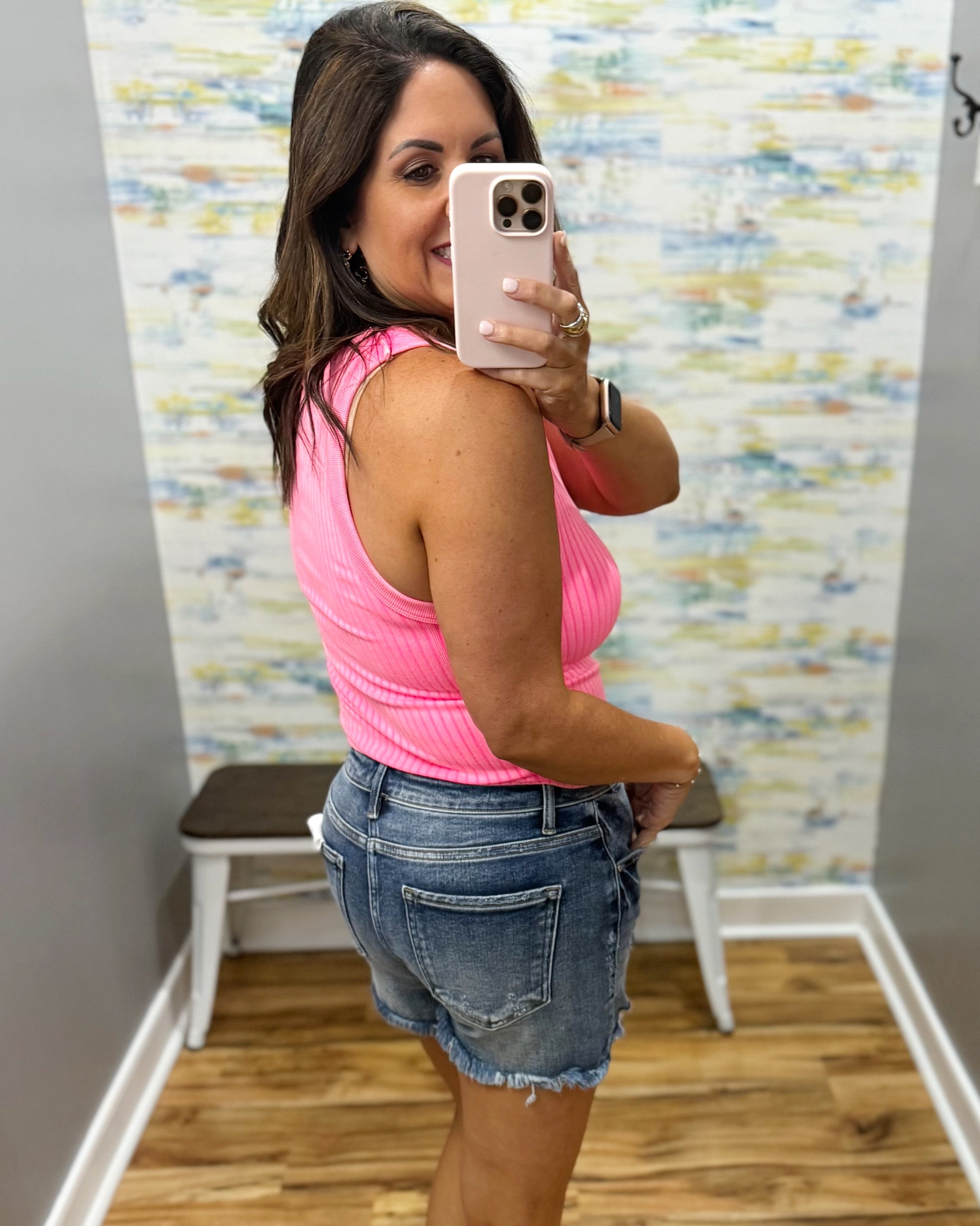 woman wearing neon coral tank with denim shorts.