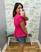 Woman taking a mirror selfie wearing a pink top and denim shorts in a room with colorful wall art.