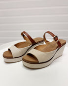 Pair of beige wedge sandals with brown straps on a white background