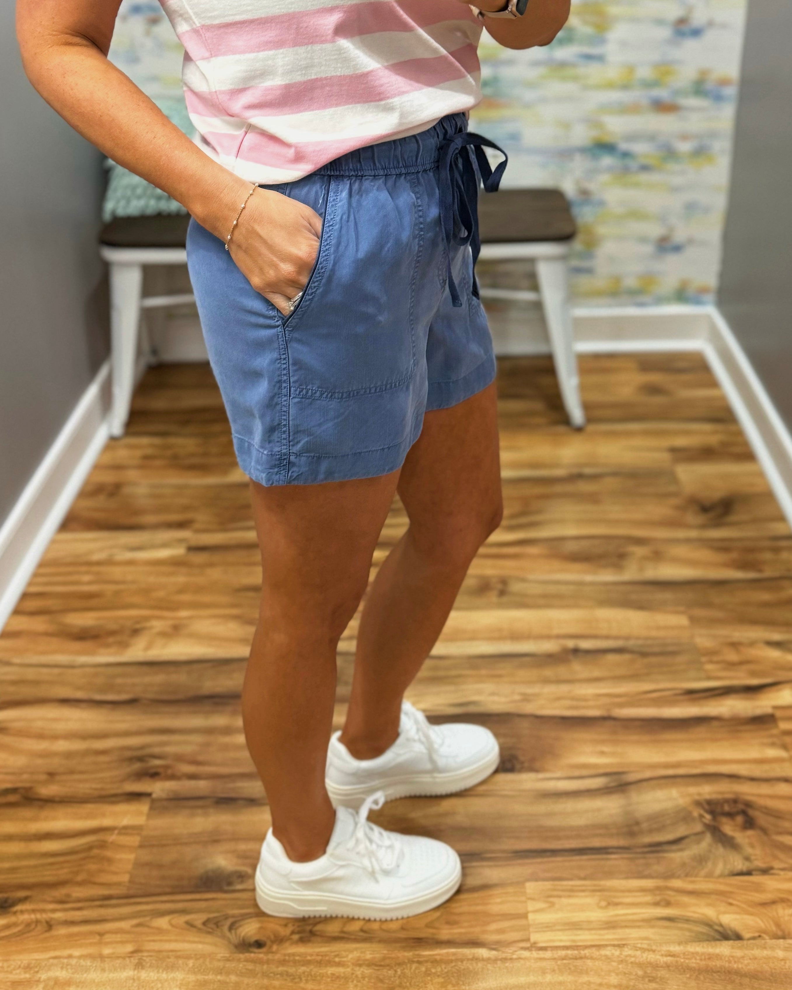 Person wearing blue shorts and white sneakers on a wooden floor.
