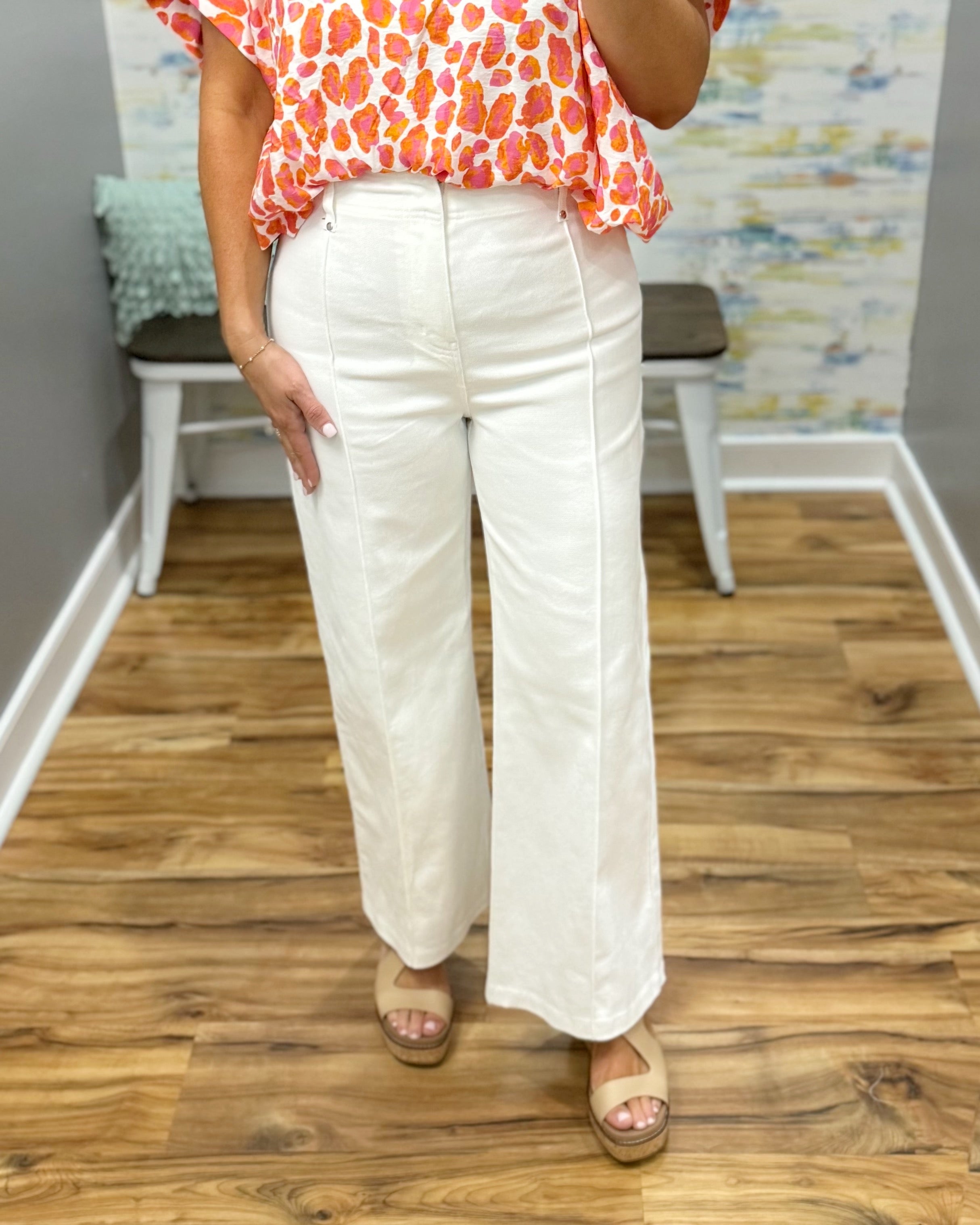 Person wearing a colorful top and white pants standing on a wooden floor.