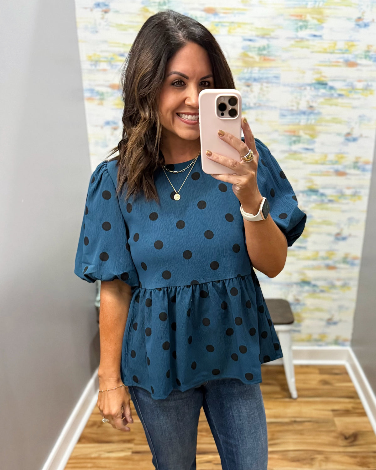 woman taking a selfie wearing a teal top with black polka dots and puff sleeves.