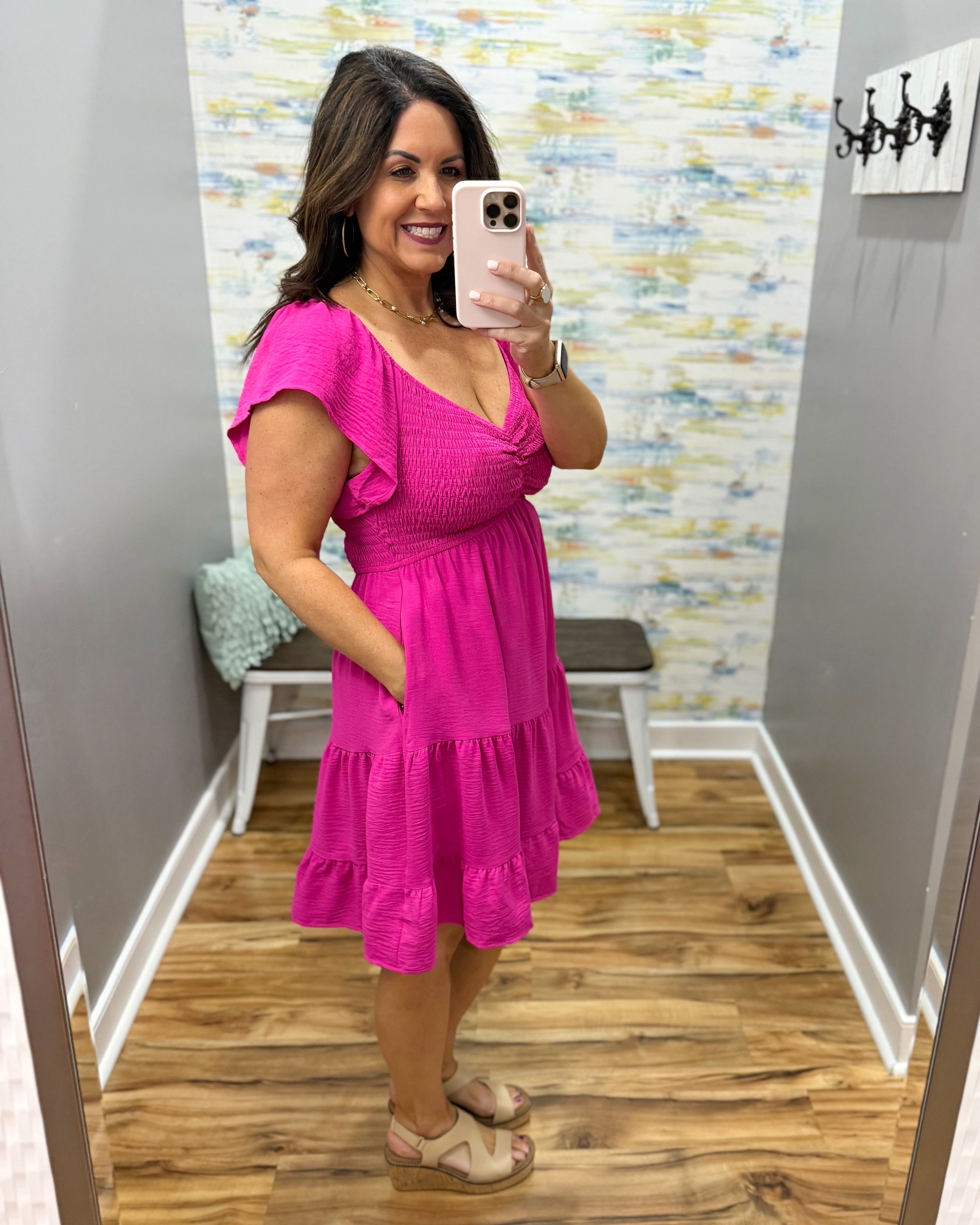 Woman taking a mirror selfie wearing a pink dress in a room with a colorful wall.