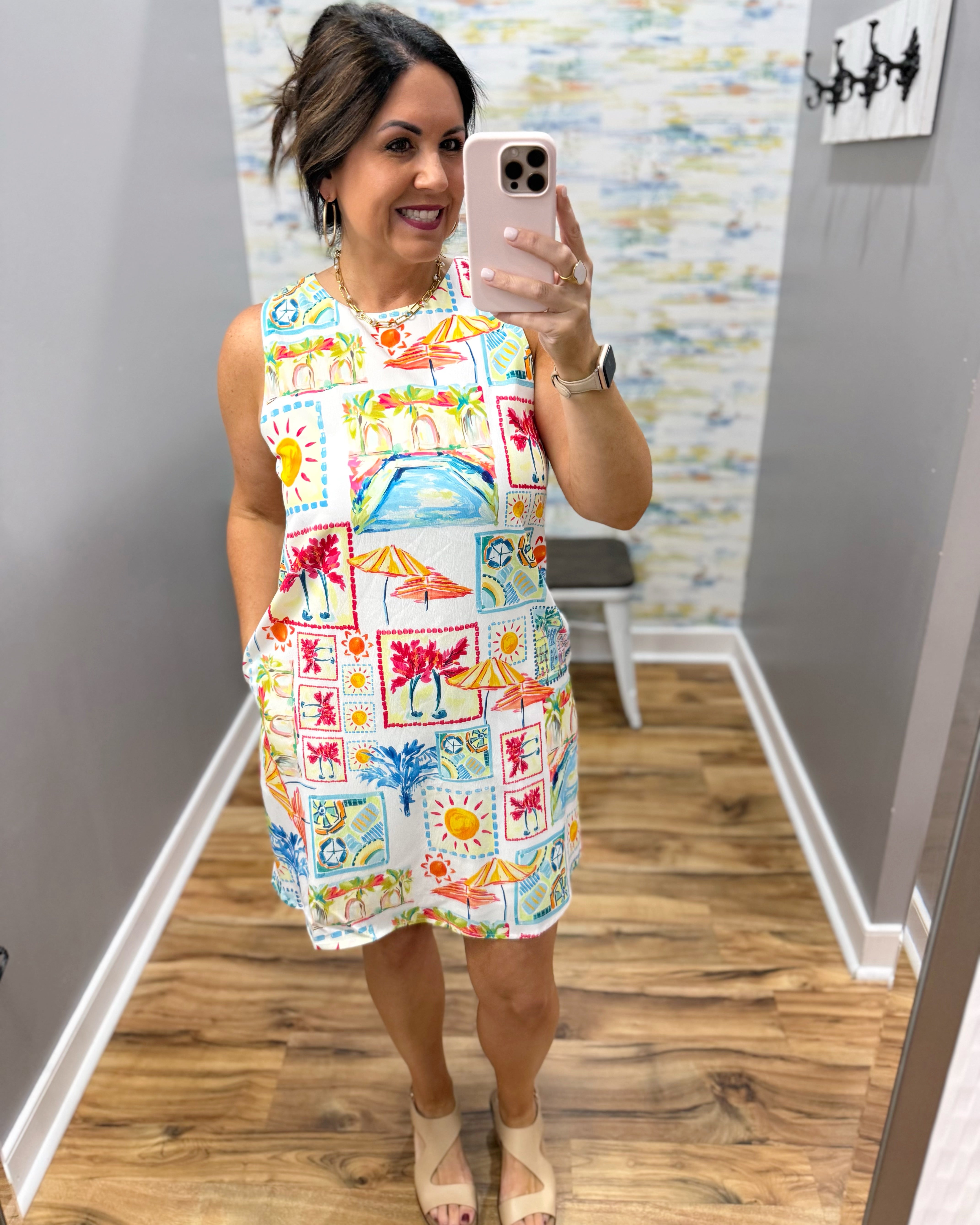 Woman taking a mirror selfie wearing a colorful dress with a pattern of beach scenes.